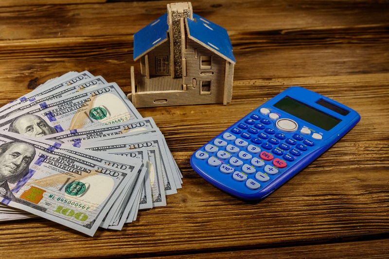 House model, U.S. one hundred dollar bills and calculator on wooden background. Property investment, home loan, house mortgage, real estate concept